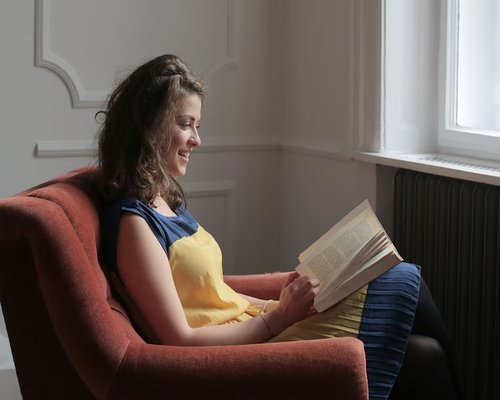 Person reading a book in a comfortable armchair near a window