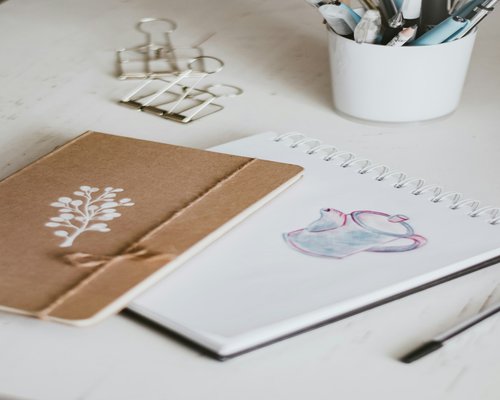 A desk with an open notebook, plant, and a cup of tea
