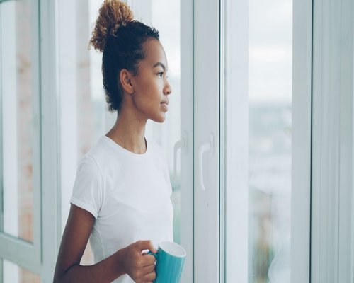 Smiling person drinking coffee and looking out the window in a bright apartment